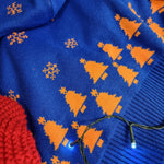 A close up the bottom hem of the jumper, it is royal blue and has knitted in orange Christmas tree shapes.