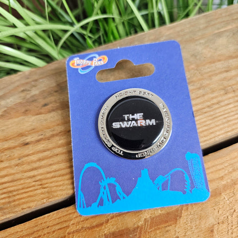 A photo of a round silver pin badge with a black insert in the middle featuring the Swarm logo