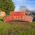 An arched sign designs to go on poles and act as an entry way. It is red with the words The Big Top in an ornate yellow font. Above the arch is a squared off section which has 'Figaro Bros Presents' writting on it in black text.