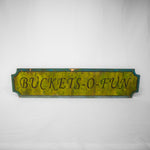 A rectangular sign with indents in each corner. The middle is a yellowy/green paint with the words Buckets-O-Fun bevelled in. The border is a teal.