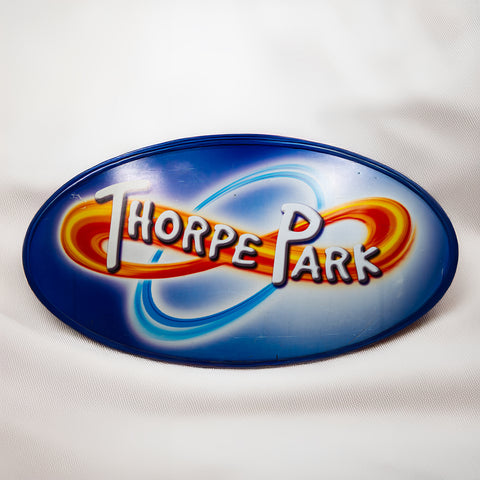 An oval shaped sign with the old Thorpe Park logo in the middle. The frame is blue.