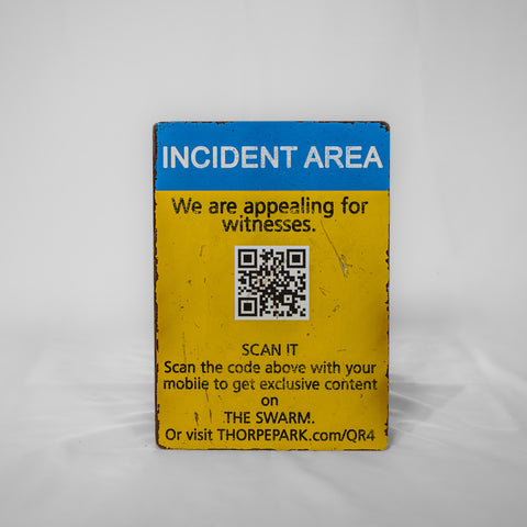 A portrait orientated sign which has a blue strip across the top with "Incident Area" inside it in white text. The lower portion is in yellow with black text reading "We are appealing for witnesses" followed by a QR code with information on how to scan it below.