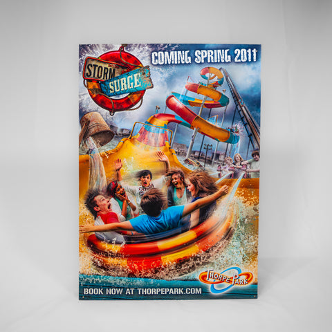 A portrait orientated poster advertising Storm Surge opening in 2011. The ride logo is in the top left corner and there is an artist impression image of people riding the ride as the main image.