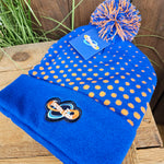 A beanie hat which is royal blue with orange dots. The bobble at the top is blue and orange wool, and an embroidered logo is on the fabric which sites on your forehead.