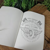 Sheet of paper with black line art design on a wooden surface with plants in the background