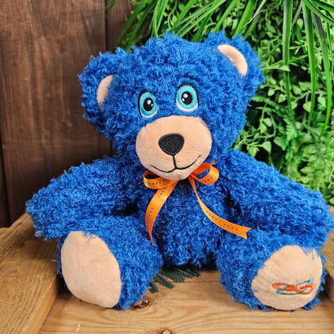 A bright blue bear with curly fur and light blue eyes. There's an orange ribbon scarf and embroidered logo on its paw