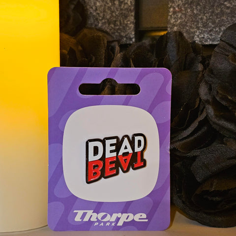 A pin badge of the DeadBeat logo, the top word "Dead" is in white, and the word "Beat is underneath it in red.