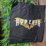 A black tote bag with the Hyperia logo printed on the middle. The logo has a metallic gold wing print with the word Hyperia in flat white on top.