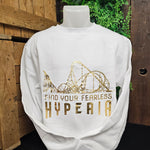 A white sweatshirt, with a gold foil print saying Find Your Fearless and Hyperia underneath. Above the text is the coaster skyline.