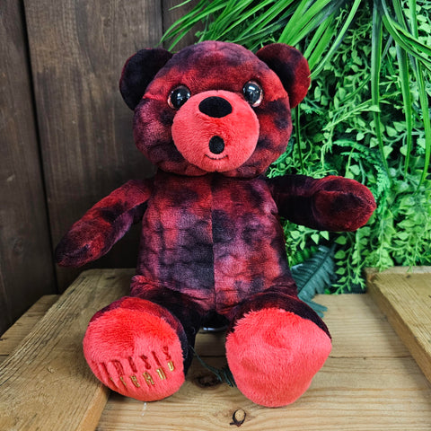 A mottled red and black bear, with a shocked face. The Nemesis Inferno logo is embroidered on the foot