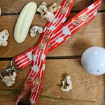 A red and white lanyard, with images of popcorn printed down it. There are some carnival logos spaced evenly along the length. Around it are some sweets