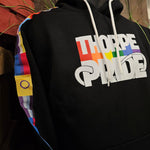 A black hoody with the Thorpe Pride logo printed in the middle. The sleeves have different pride flags down the arms on a stitched on tape.