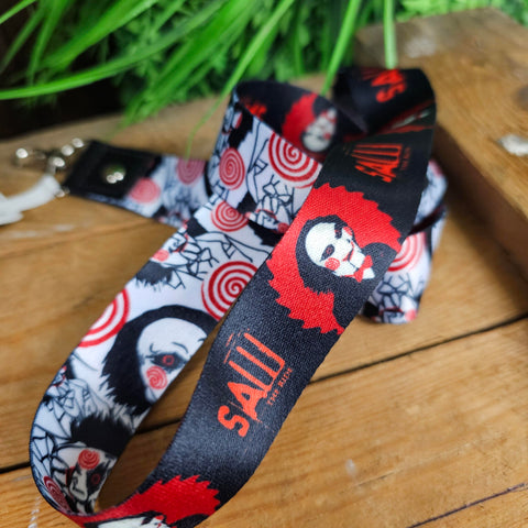 A lanyard with a white side featuring Billy's face and red spirals, and a black side with the ride logo and billy in a red circular saw shape.