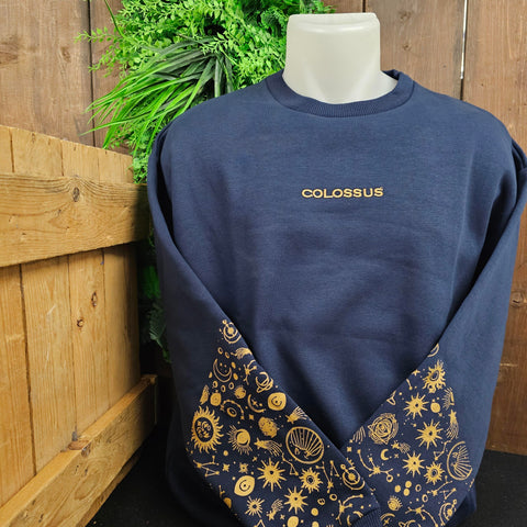 A royal blue sweatshirt with the word Colossus embroidered on the chest in a gold thread, and a cosmic pattern on the lower half of the sleeves