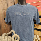 A photograph of the tshirt, it is a blue/grey colour but acid washed so the colouring is patchy giving a distressed look. The Stealth logo is embroidered on the front in a grey thread