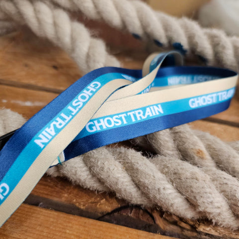 A three tone lanyard in cream, teal and royal blue. Along the teal stripe is the words Ghost Train in white text