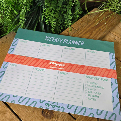 Weekly planner with a colorful design on a wooden surface with plants.