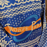 A close up of the knitted logo on the middle of the jumper, it is blue with a white snow detail, and an orange loop in the middle