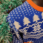 A close up of detail on the shoulder of the jumper, it is blue with white snow and Christmas tree shapes. The jumper collar is solid orange.
