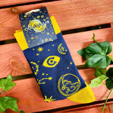 A photo of a pair of socks in their packaging. The socks are royal blue, with vibrant yellow ankles, toes and heel areas. In the middle of the blue are yellow constellation symbols.