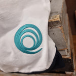 A photograph of the embroidered logo on the base of the t-shirt, it is a teal colour on a white background