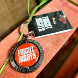 A photograph of the keyring, it is round with an outer circle in a grey metal. The inner circle is red with the Fright Nights logo on it. Around the outer metal circle is "The Home Of Fear"