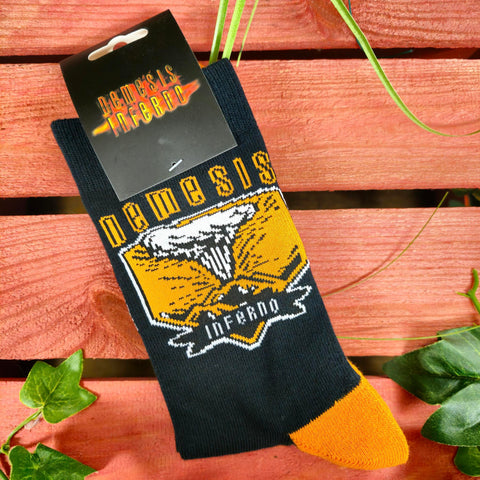 A pair of socks in the packaging, they are black with an orange and white graphic on the middle and orange heels and toes.