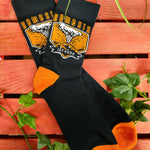 A pair of socks without packaging, they are black with an orange and white graphic on the middle and orange heels and toes.