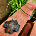 A photo of a jigsaw puzzle piece shaped magnet, it is black with red text saying "I want to play a game"
