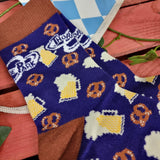 A photograph of the socks out of packaging. The main sock is a dark blue colour, and there are brown details on the heel and ankle areas. The patter is repeat beer steins (cream and yellow coloured), and pretzels (brown with white salt fleck detail). At the top in white is the Thorpe Park logo.