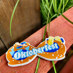 A magnet which has a brown pretzel shape behind it, with the word Oktoberfest in the middle in white text with a light blue outline. On the top left corner is the Thorpe Park logo, and on the right corner are two yellow beer steins