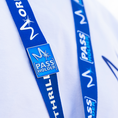 A photograph of the Pass Holder pin badge on a lanyard. It is a shiny royal blue with silver lettering and the letter "m" symbol at the top.