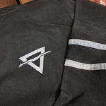 A close up photograph of the embroided symbol, it is light grey and the shape of a triangle with a horizontal line through it. The top behind is black.