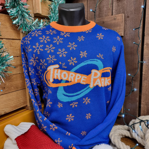 A photograph of a knitted jumper, it is in a royal blue with orange detailing on the collar and cuffs. There are orange snowflakes embroidered into the right hand shoulder. In the middle is a Thorpe Park logo.