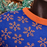 A close up of the shoulder detailing of the jumper. It is orange snowflakes on a royal blue knitted base. The orange collar is also visible.