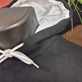 A close up photograph of the hoody, the fabric is black with white lining in the hood and white cords