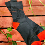 A photo of a pair of socks. The socks are dark grey with black tyre print, there's a Stealth logo on the ankle area with red lines above and below it. The heels and toes are red.