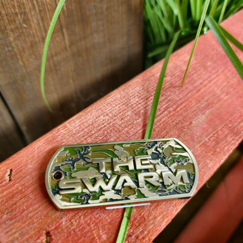 A rectangular magnet with rounded ends. The infill is camo print, with the words The Swarm and the edges in a raised silver metal.