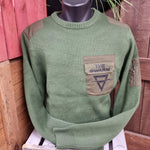 A photograph of a knitted jumper in a moss green colour, there is a pocket on the top left chest area with The SWARM logo on it.
