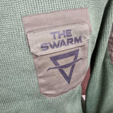 A close up of the popper pocket with The SWARM logo on. It is a camo green, on a moss green knitted base.