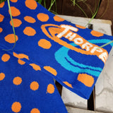 Another angle of the logo knitted into the scarf, the background is dark blue with orange dots