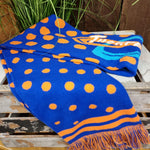A photograph of a scarf, it's base colour is a royal blue with orange dots. At the ends are blue and orange tassels, in the middle is a Thorpe Park logo