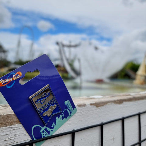 A photograph of the pin badge in front of Tidal Wave which has caused a large splash of water